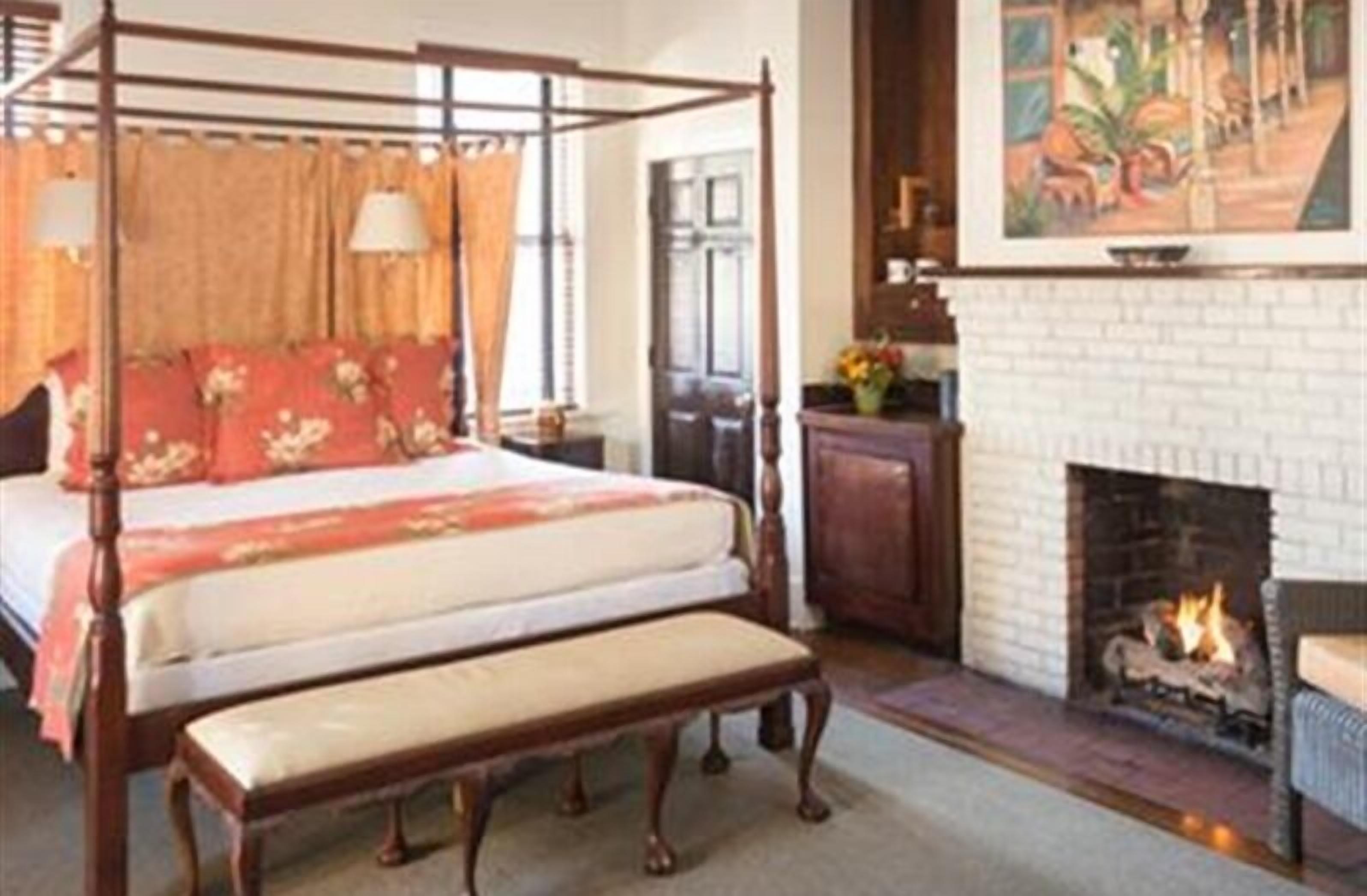 A four-poster bed with a bench, a fireplace, and a painting above it.
