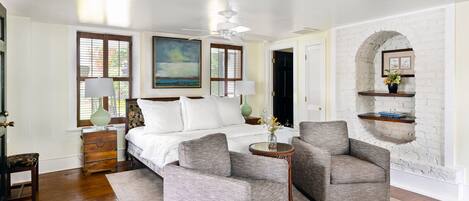 A bedroom with a bed, two armchairs, a small table, and a white brick wall.
