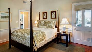 A four-poster bed with floral bedding, a bedside table with a lamp, and framed botanical prints on the wall.