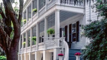 A white colonial-style building with a covered porch, columns, and a sign reading "The Rhetorical House Inn".