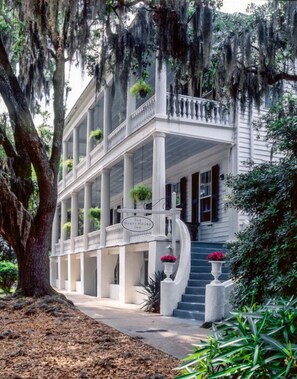 A white colonial-style building with a covered porch, columns, and a sign reading "The Rhetorical House Inn".