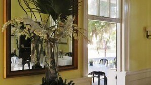 A hallway with a large mirror, a vase with flowers, and a view of an outdoor dining area. - Rhett House Inn (Beaufort)