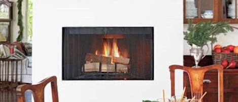 A dining area with a fireplace, a table set for two, and a bookshelf in the background.