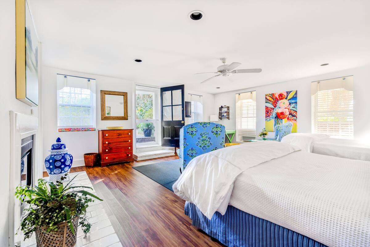 Une chambre à coucher avec un grand lit, une commode, une chaise, un ventilateur de plafond et une fenêtre avec des stores.