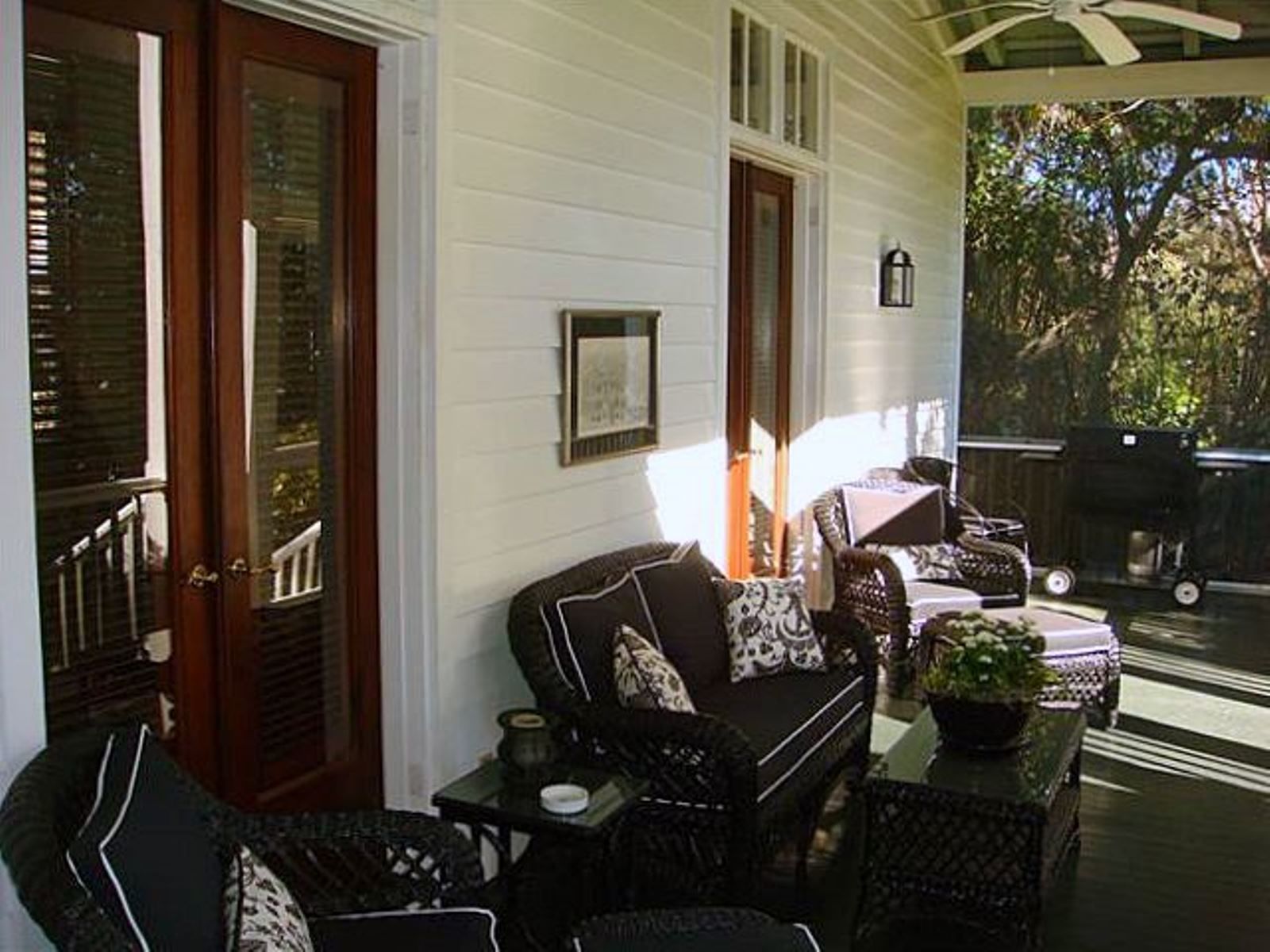 A covered porch with wicker furniture, a small table, and a potted plant.