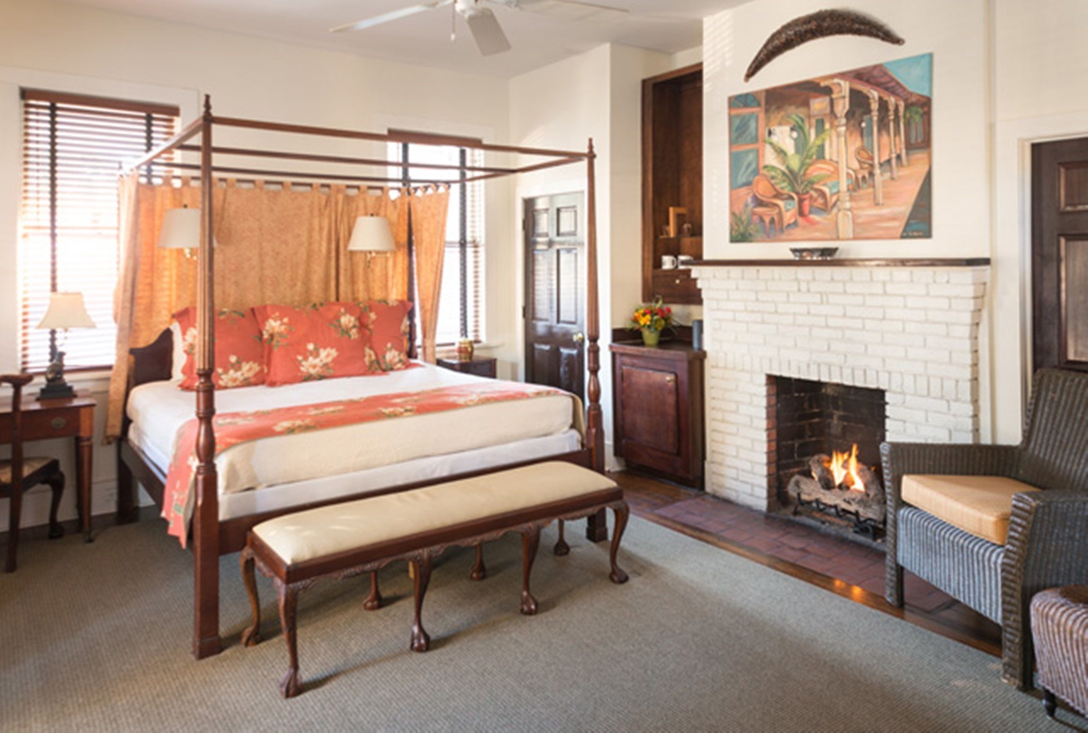 A four-poster bed with a bench, a fireplace, and a painting on the wall.