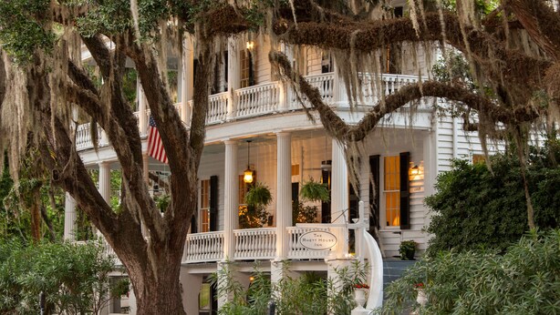 A historic building with a balcony, large trees, and an American flag. - Rhett House Inn (Beaufort)