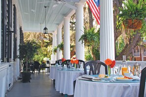 A covered outdoor dining area with white columns, tables set with plates, glasses, and flowers.