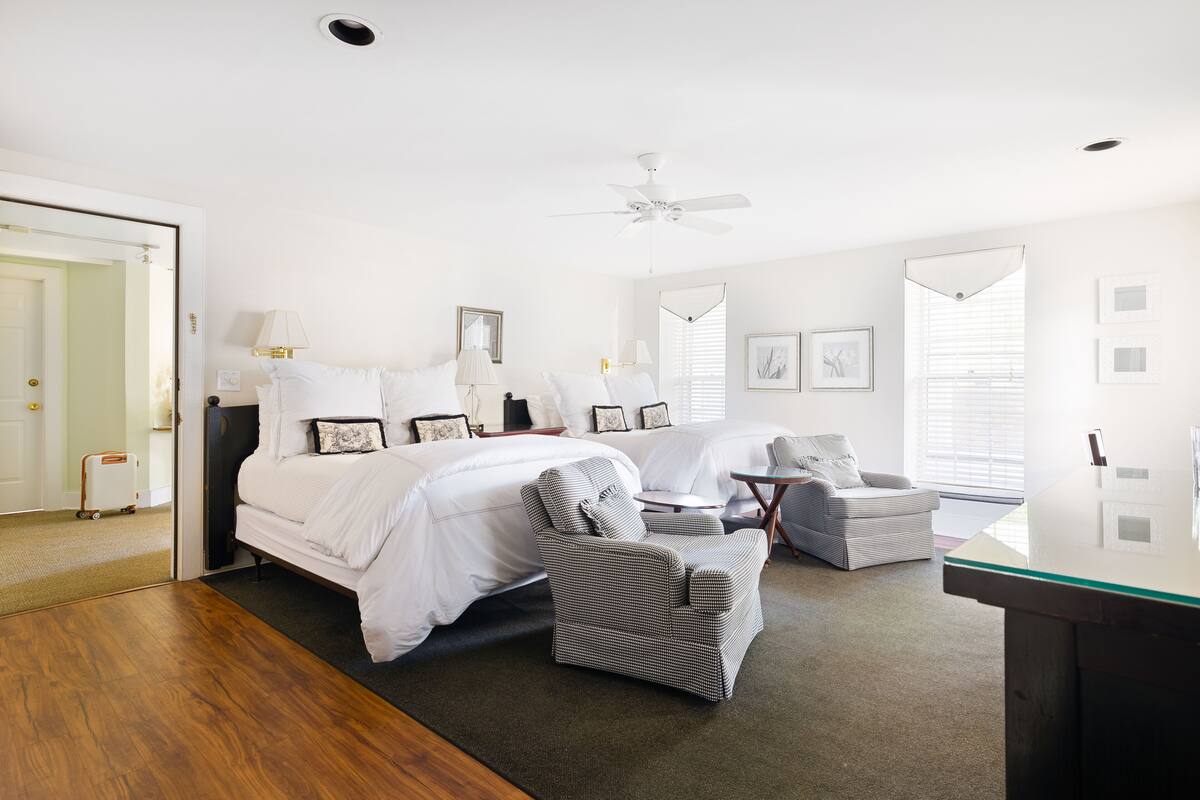 Une chambre spacieuse avec un grand lit, une chaise, un bureau et un ventilateur de plafond.