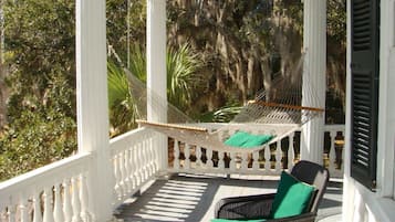 A porch with a white balustrade, a wicker chair with a green cushion, and a hammock.