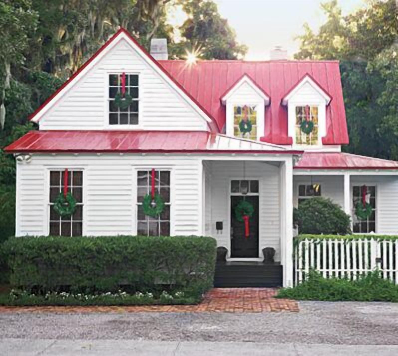 A white house with a red roof, a front porch, and a picket fence.