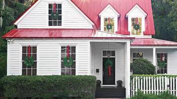A white house with a red roof, a front porch, and a picket fence.