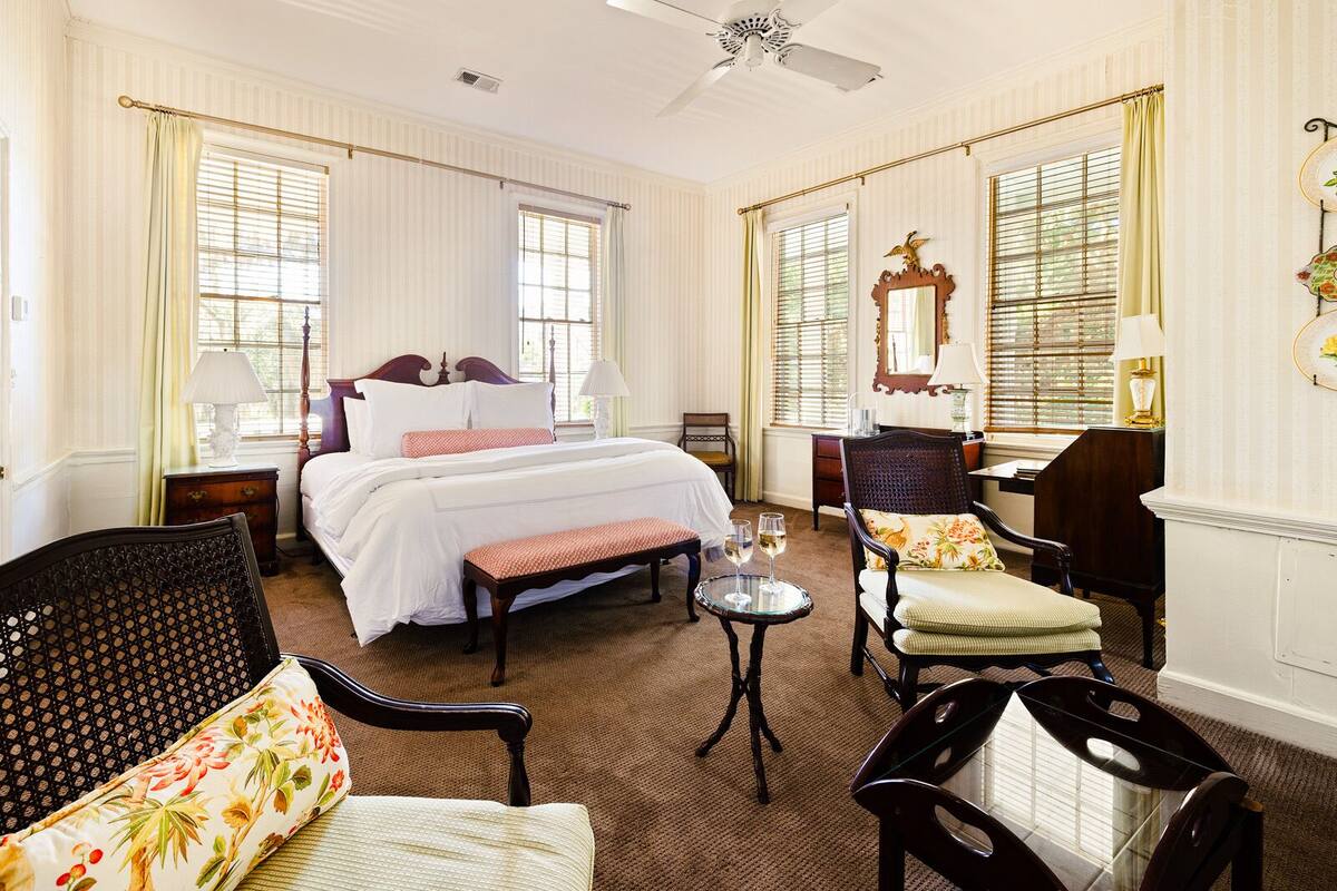 Une chambre d’hôtel avec un grand lit, un coin salon avec une table et des chaises, et un bureau avec une lampe.