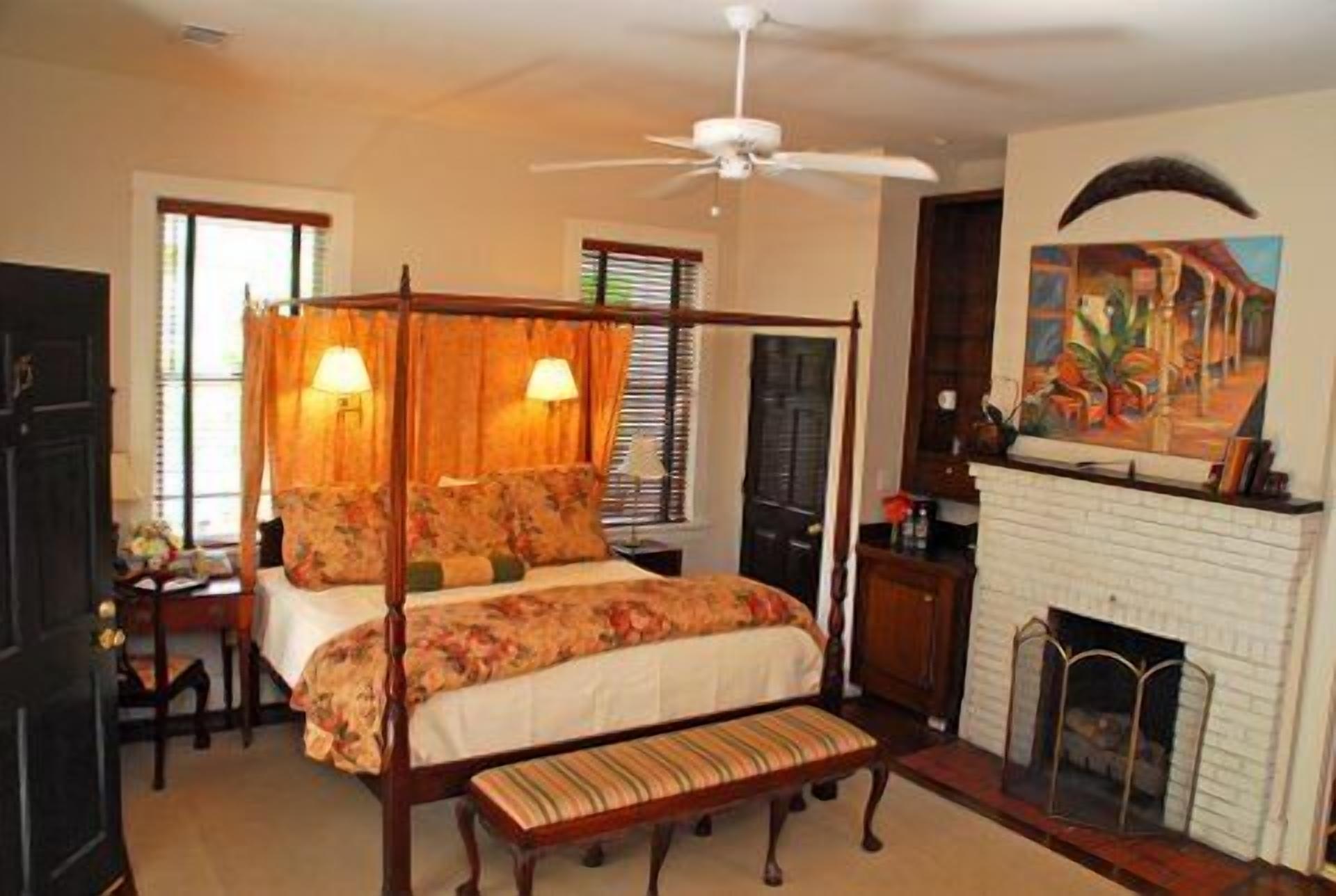 A bedroom with a four-poster bed, a fireplace, and a ceiling fan.