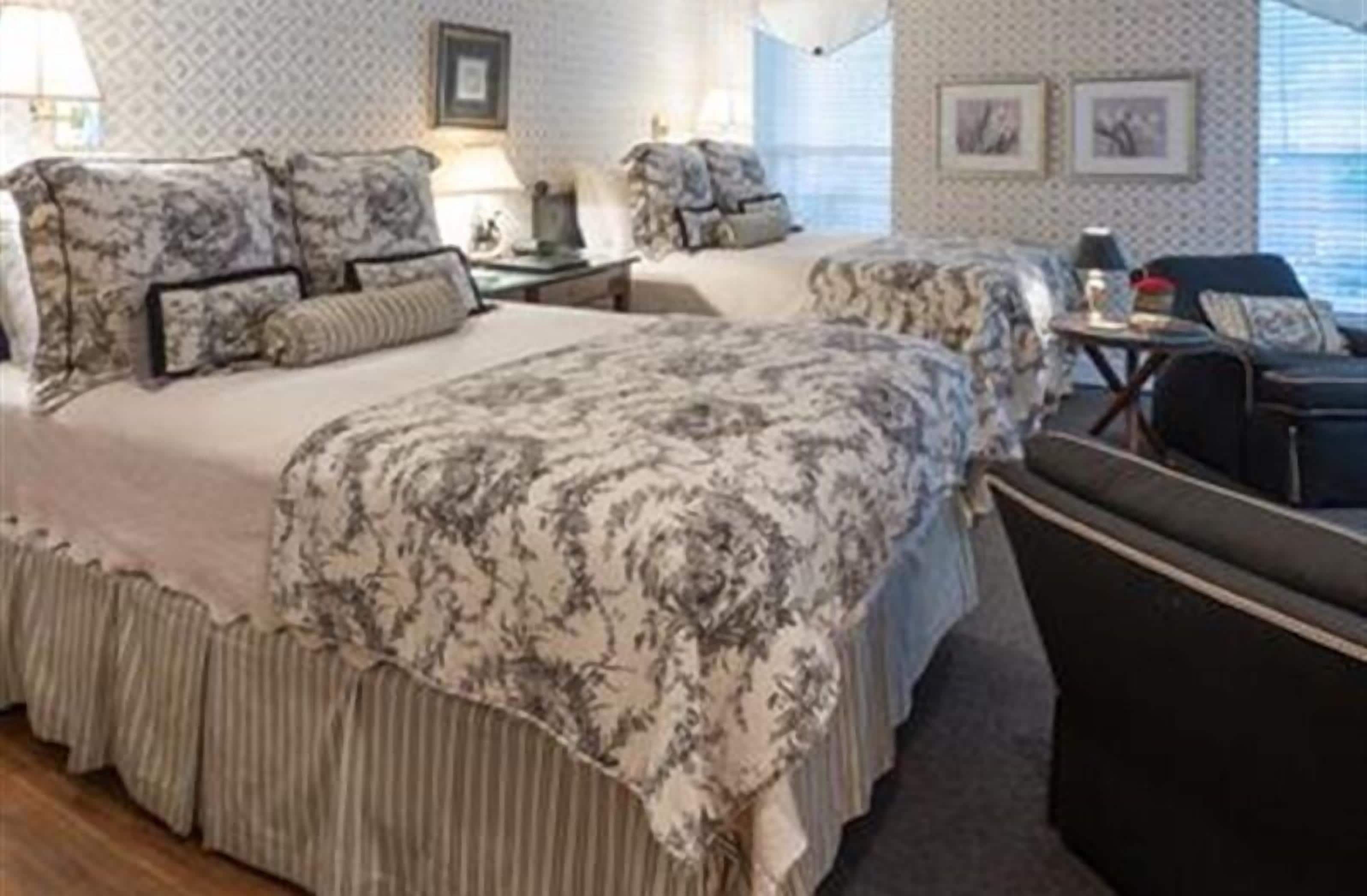 A hotel room with two beds, a small table, a chair, and a window with blinds.