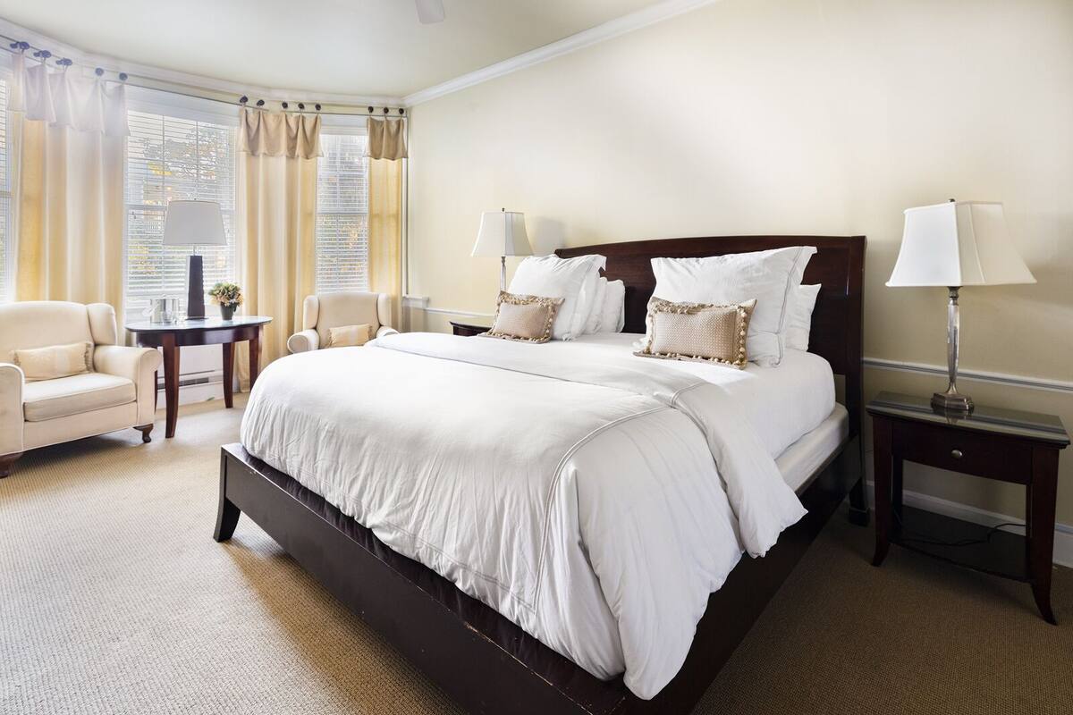 Une chambre d’hôtel avec un grand lit, deux tables de chevet avec des lampes, un canapé et une petite table sur laquelle est posé un vase.