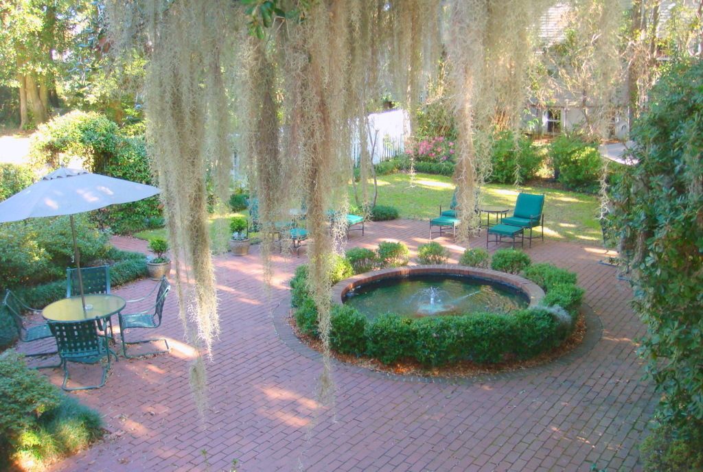 A garden patio with brick flooring, a circular fountain, and green chairs.