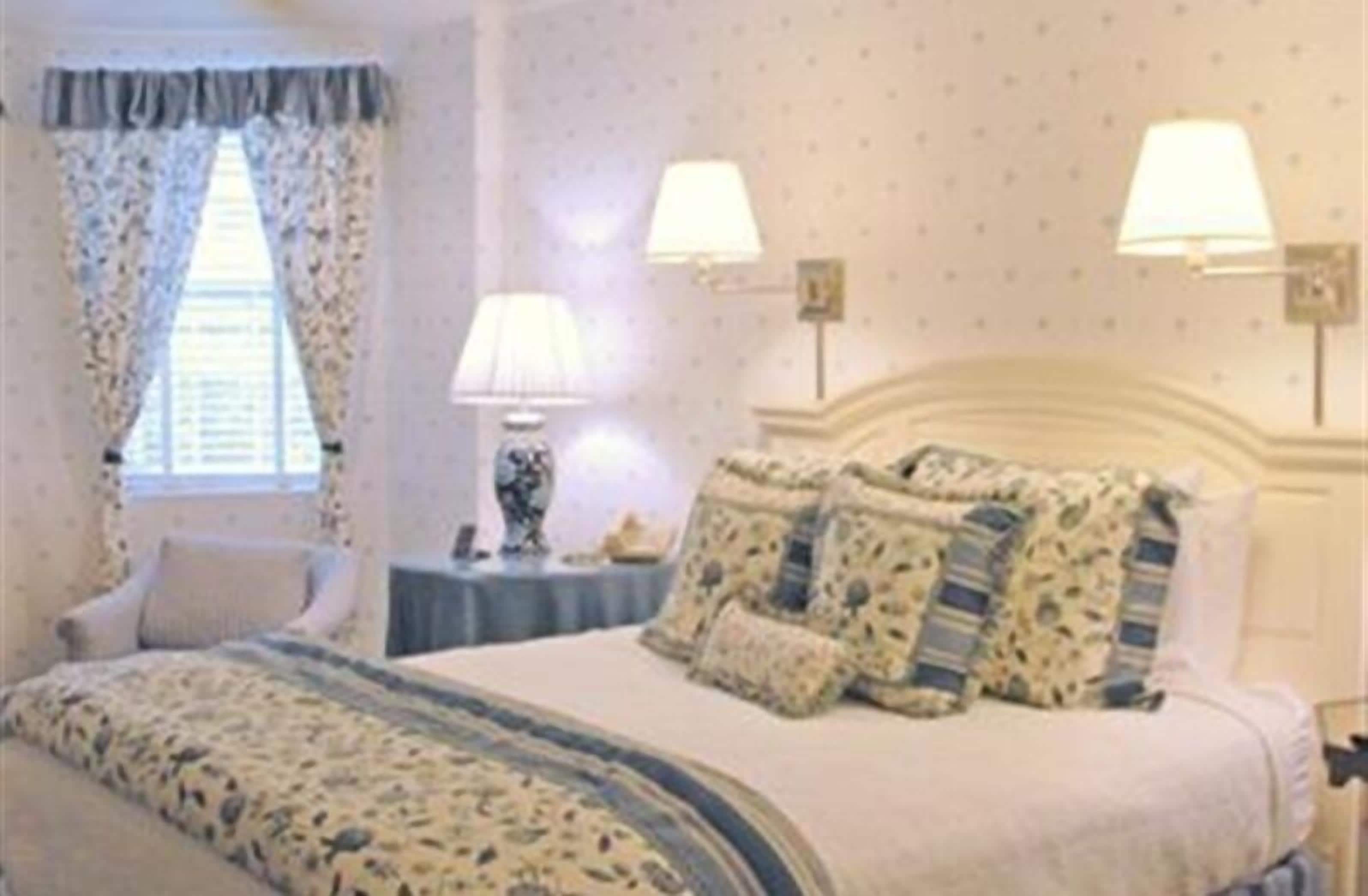 A bedroom with a bed, two bedside lamps, a nightstand, and a chair.