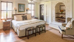 A bedroom with a large bed, two bedside tables, a chair, a fireplace, and a ceiling fan. - Rhett House Inn (Beaufort)