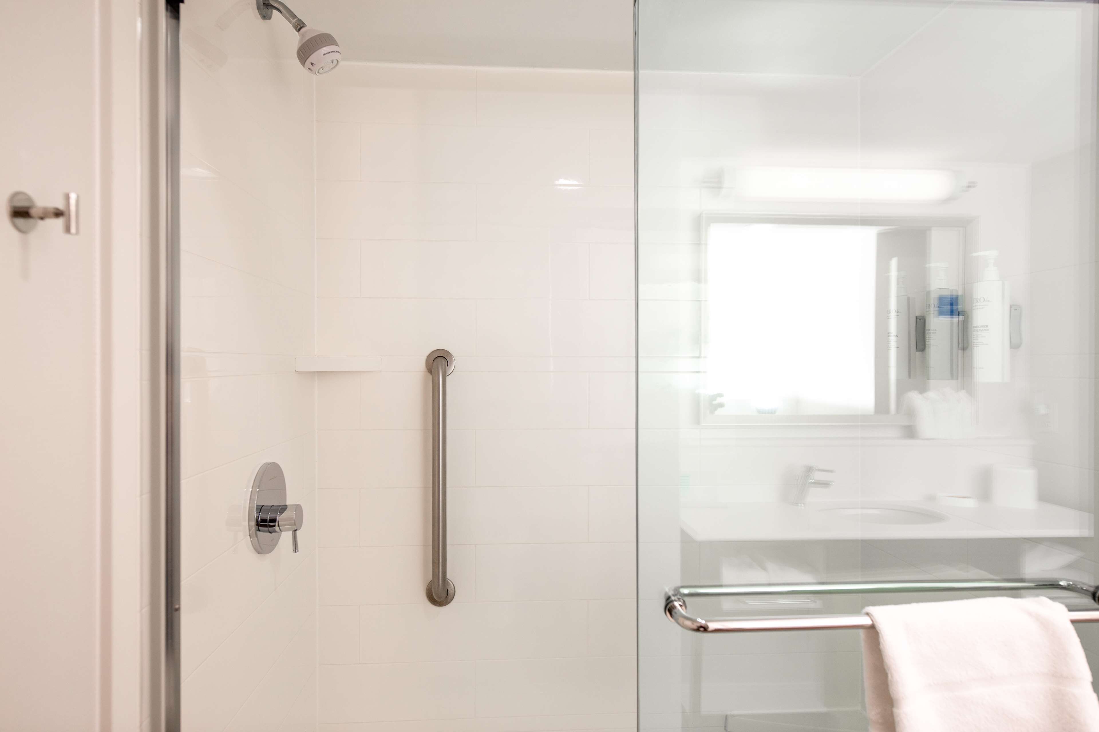 Un baño moderno con cabina de ducha de vidrio, barra de apoyo y puerta de cristal.