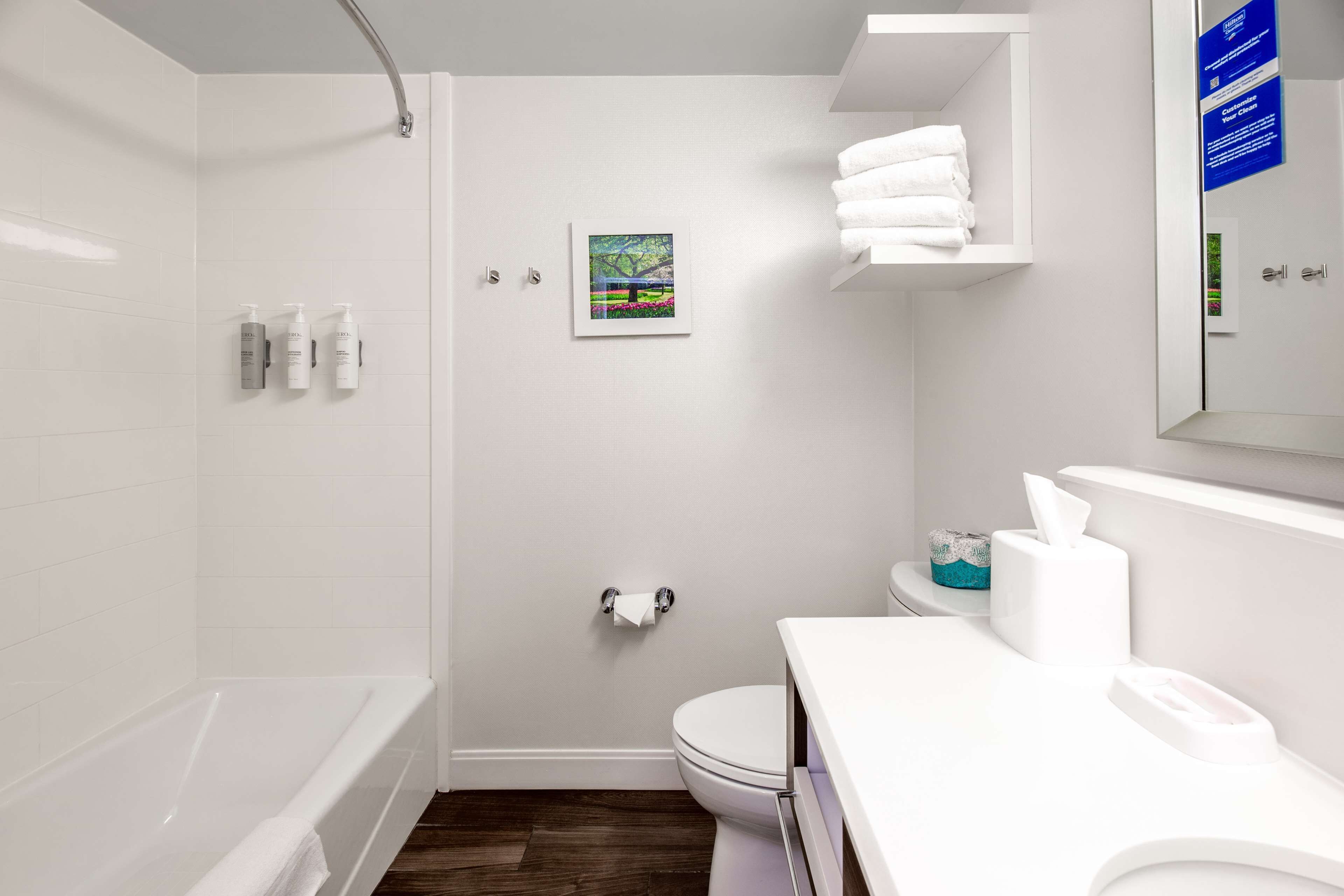 Un baño moderno con bañera, inodoro y lavamanos. Hay artículos de aseo en la pared y un perchero.