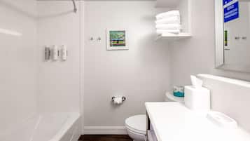 Un baño moderno con bañera, inodoro y lavamanos. Hay artículos de aseo en la pared y un perchero.