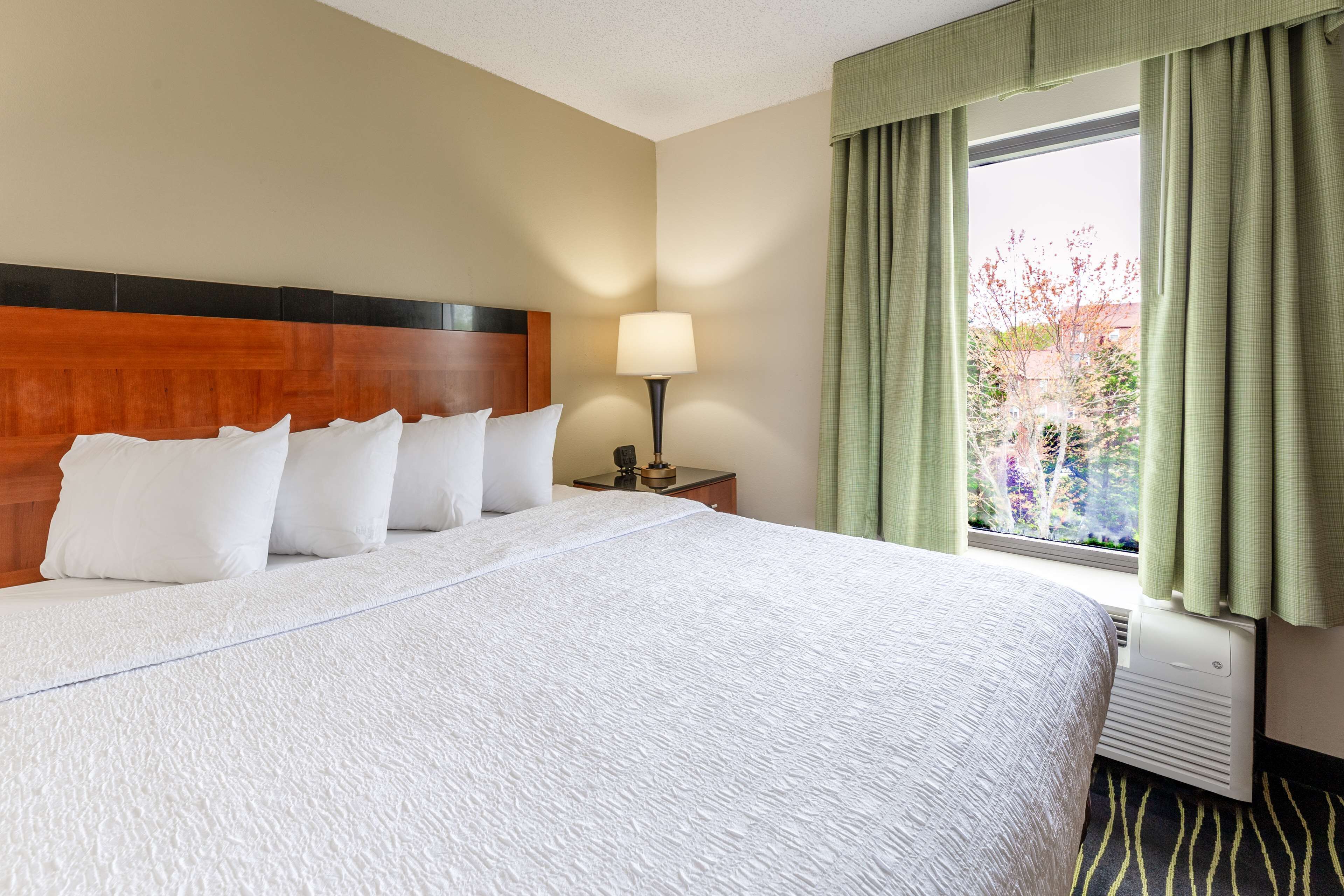 A hotel room with a large bed, a nightstand, a lamp, and a window with curtains.