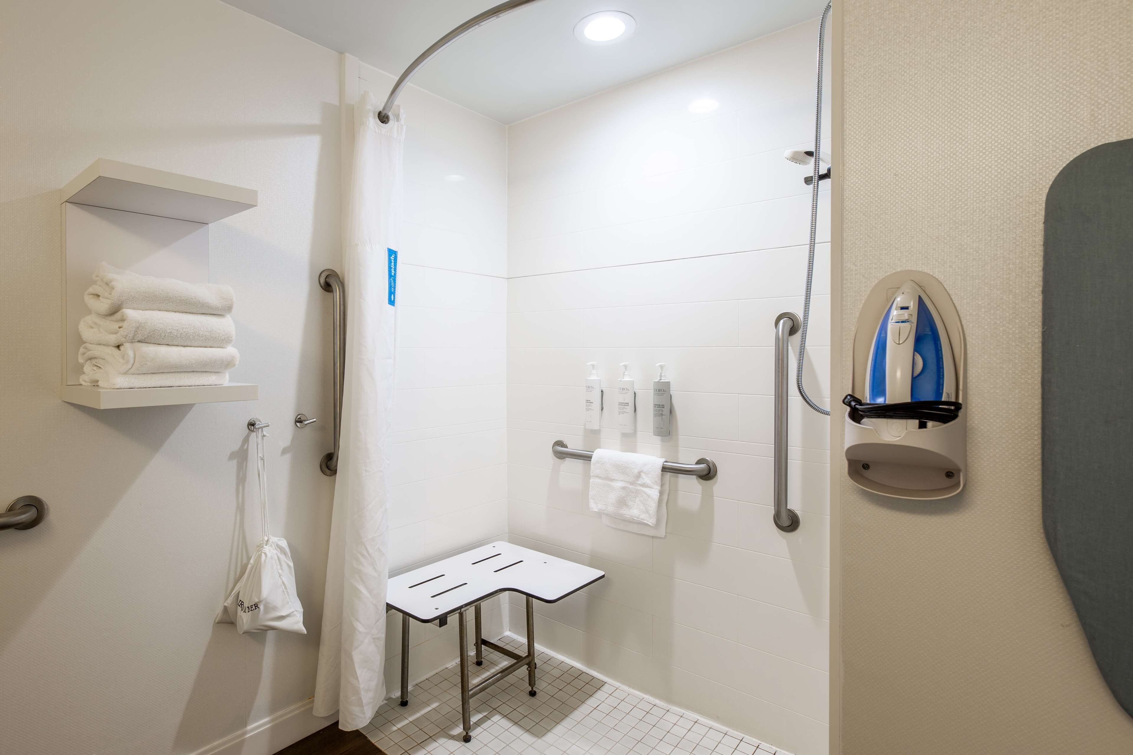 A modern bathroom with a shower, a white towel rack, a small table, and a towel hanging on the wall.