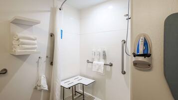 Un baño moderno con ducha, un toallero blanco, una mesita pequeña y una toalla colgada en la pared.