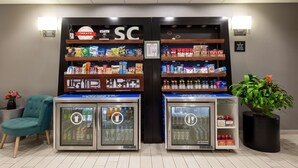 Un espace de libre-service proposant des boissons, avec des distributeurs réfrigérés, des étagères de snacks et un coin salon agrémenté d’un fauteuil de couleur turquoise.