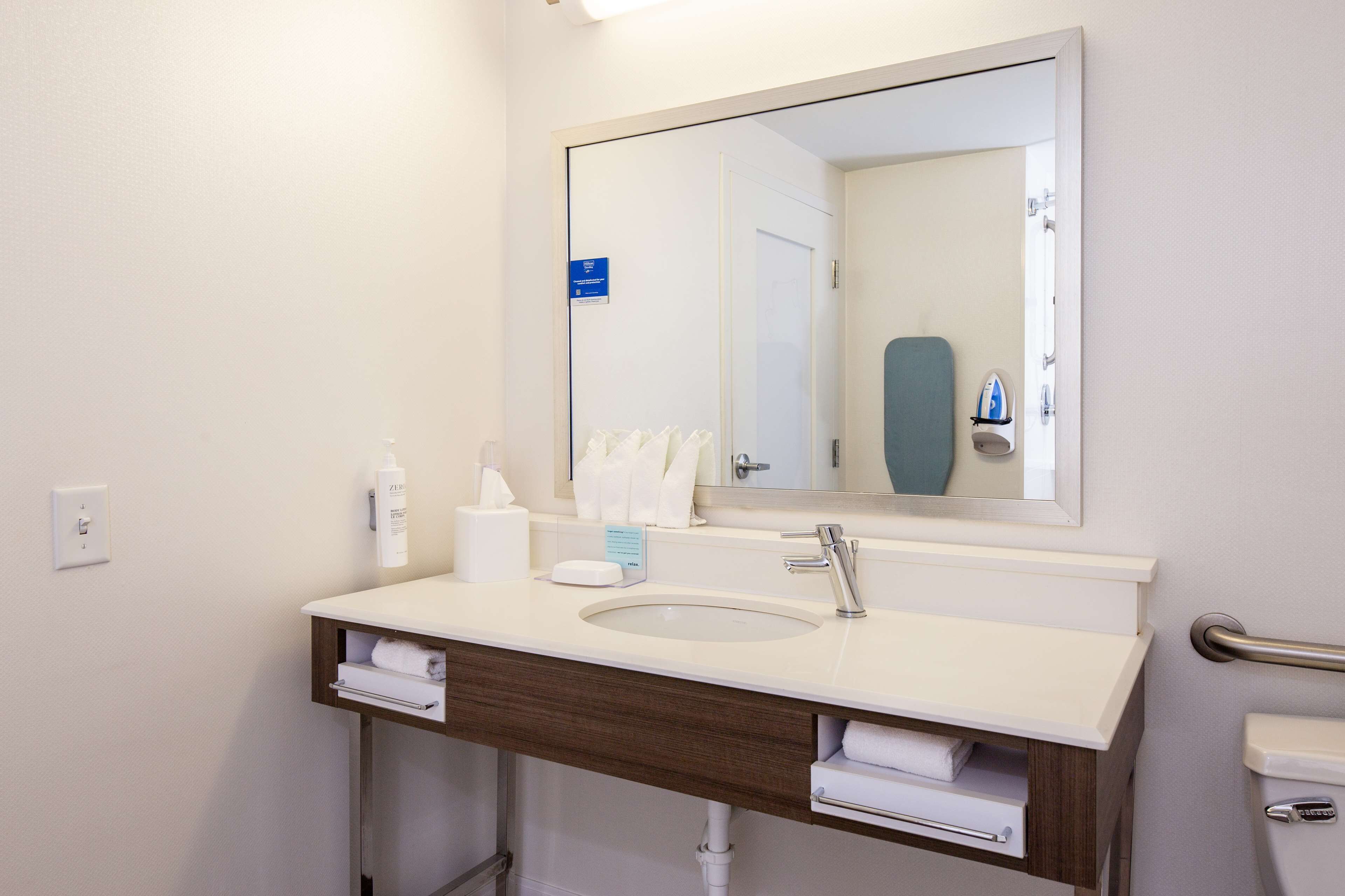 A modern bathroom with a white sink, a large mirror, and a towel rack.