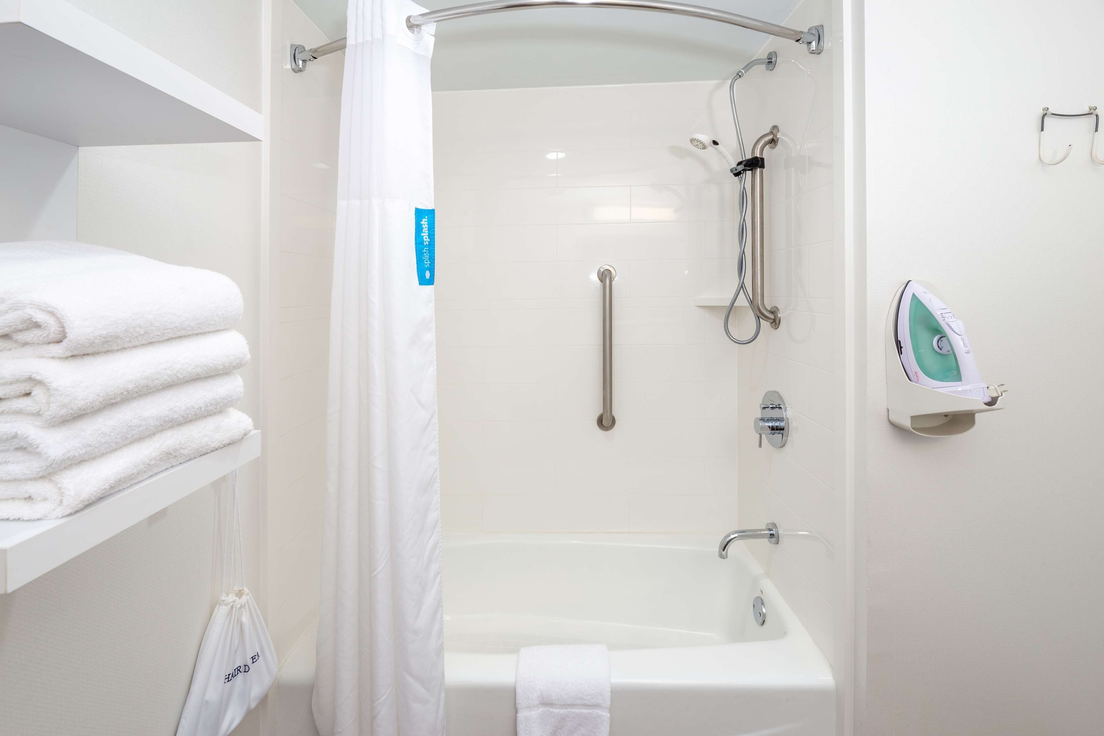 Ein modernes Badezimmer mit einer Badewanne, einer Dusche mit Glastür, einem Handtuchhalter und einem Bügeleisen.