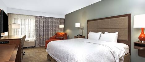 Una habitación de hotel con una cama grande, un escritorio, una silla, un televisor y una lámpara.