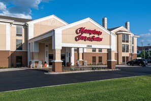 A Hampton Inn & Suites hotel with a beige facade, large windows, and a prominent entrance.