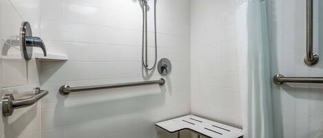 A bathroom with white tiled walls, a shower with a handheld showerhead, grab bars, and a small bench.