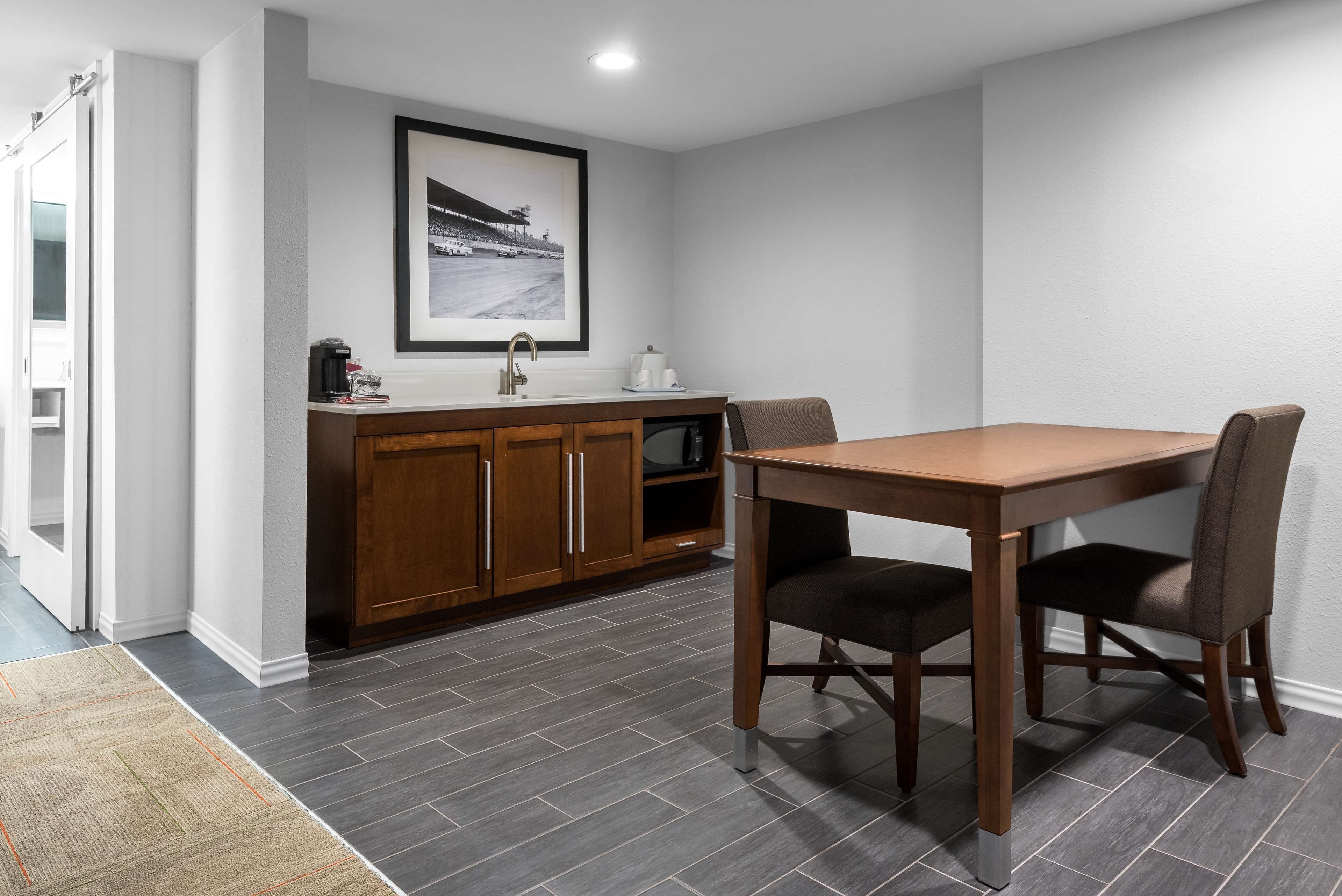 A modern kitchen with a wooden table and chairs, a sink, and a framed picture on the wall.