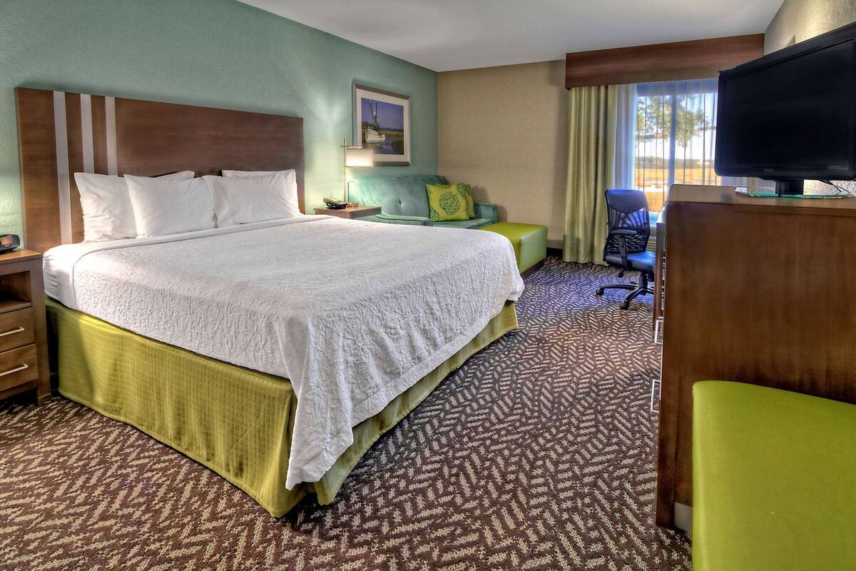 A hotel room with a large bed, a television, a desk, and a chair.