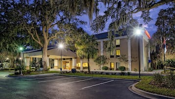 Un hotel con fachada moderna, estacionamiento y jardines bien cuidados.