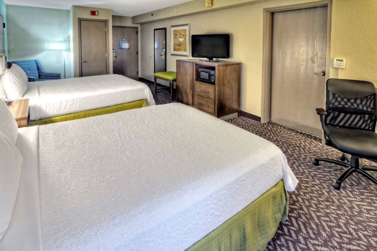 A hotel room with two beds, a desk with a computer, a television, and a chair.