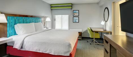 A hotel room with a bed, a desk, a chair, a TV, and a window.
