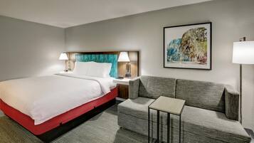 A hotel room with a bed, a sofa, a small table, and a painting on the wall.