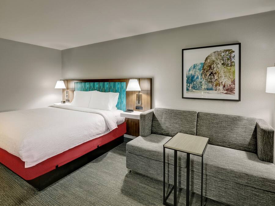 A hotel room with a bed, a sofa, a small table, and a painting on the wall.