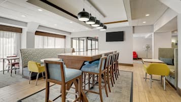 Un moderno vestíbulo de hotel con zona de comedor central, diferentes disposiciones de asientos y un amplio ventanal con vistas.