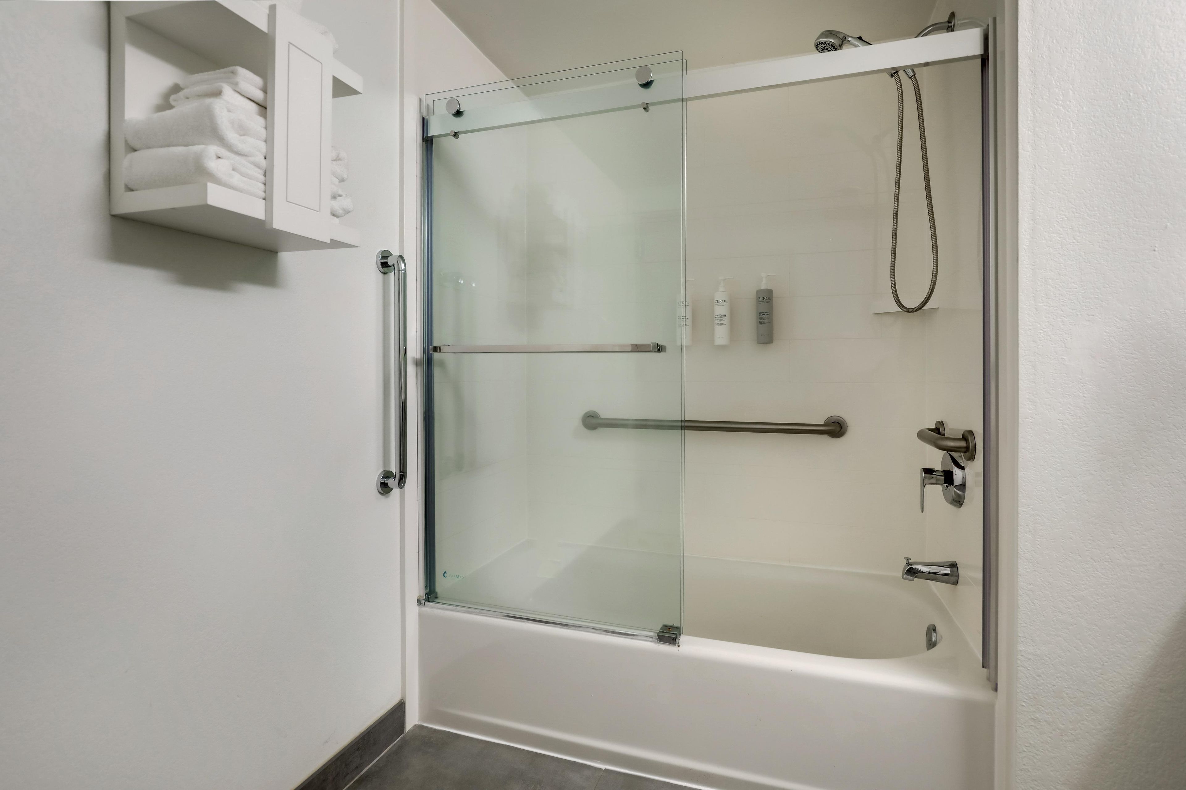 Ein modernes Badezimmer mit einer gläsernen Duschkabine, einer Badewanne und einem Ablagebereich mit ordentlich gefalteten Handtüchern.