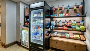 Un expositor refrigerado con diversas bebidas y aperitivos, estantes con productos envasados y una encimera de madera con artículos adicionales.