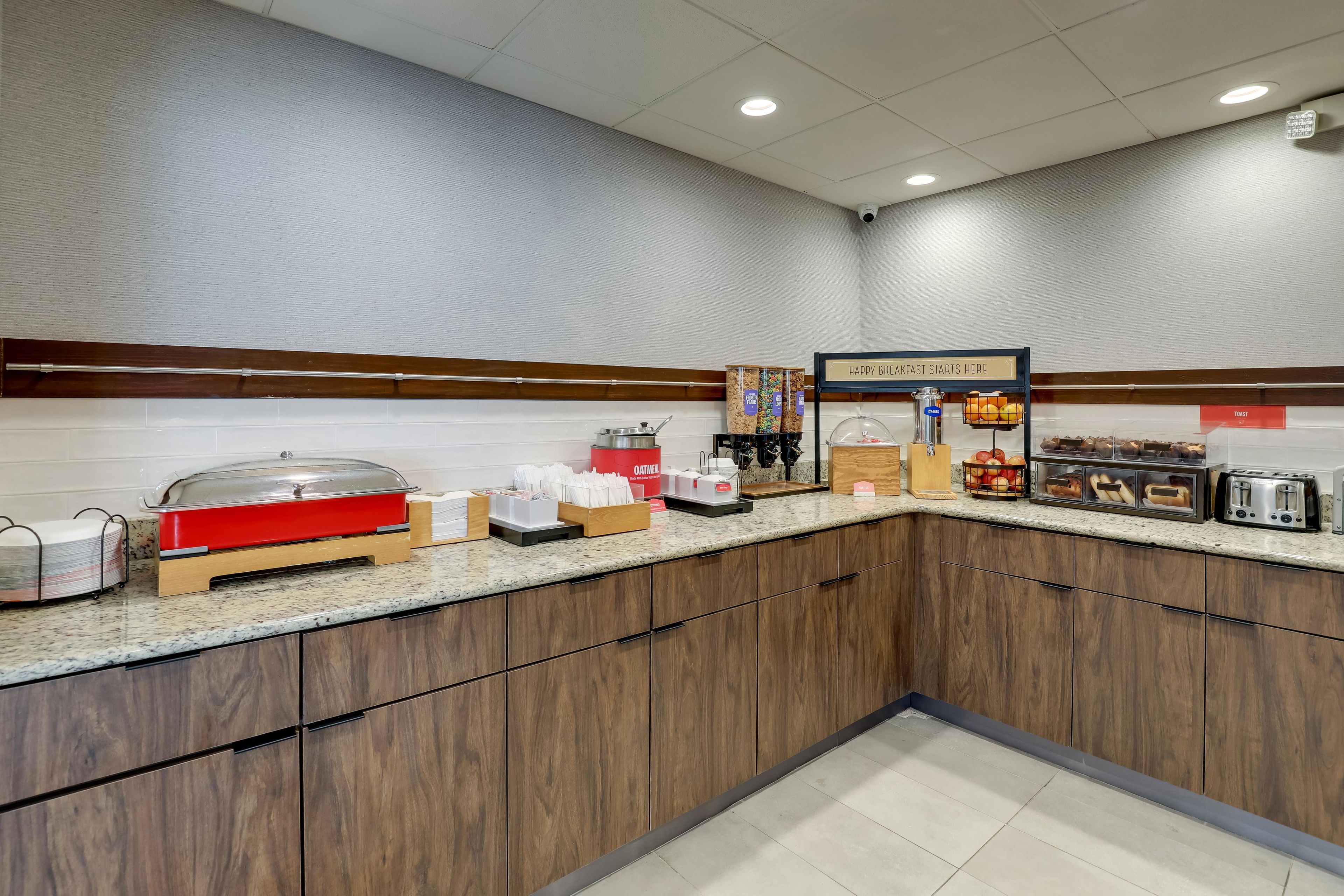 A breakfast buffet area with various food items, a coffee machine, and a sign indicating the start of breakfast.