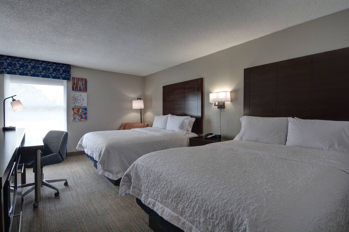A hotel room with two beds, a desk, and a chair.
