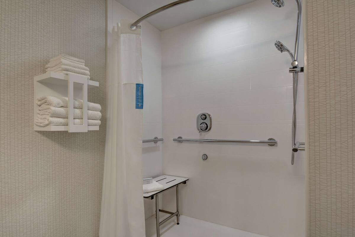 A walk-in shower with a grab bar, a towel rack, and a small table with a towel.