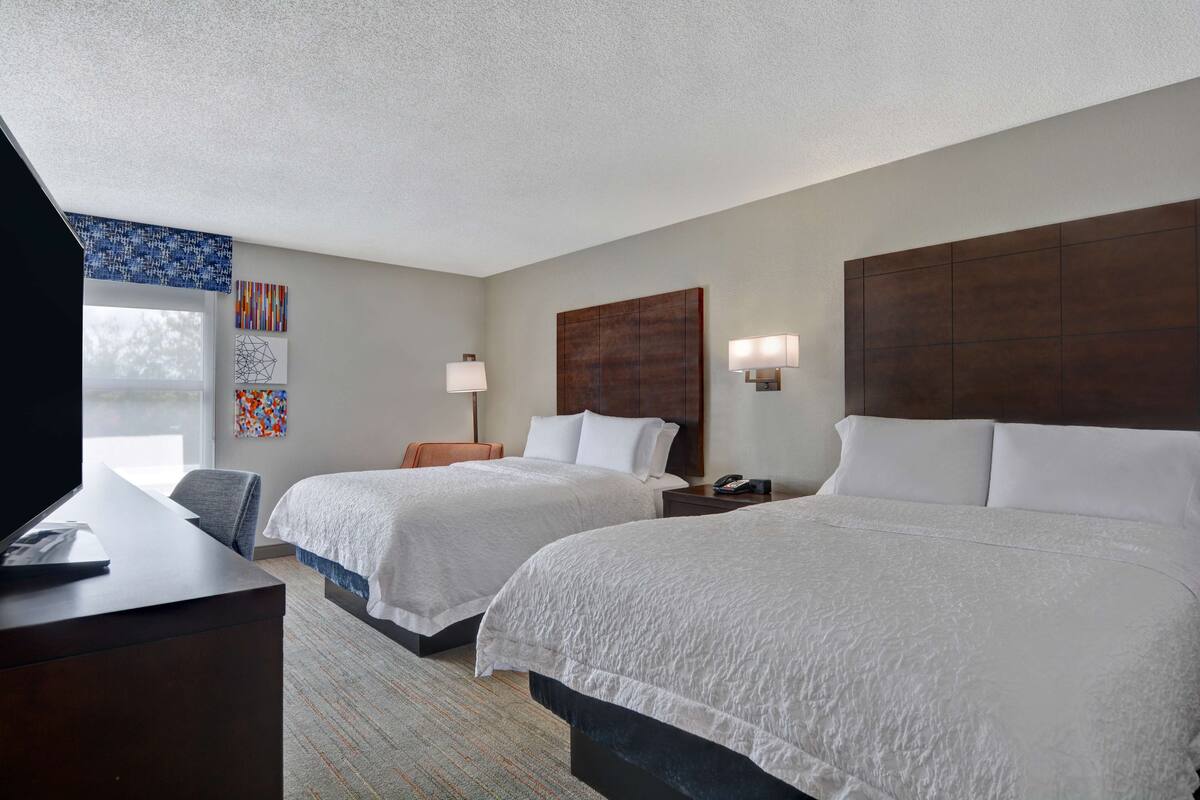 A hotel room with two beds, a desk with a computer, a chair, and artwork on the walls.