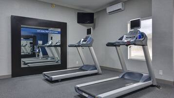 A gym with three treadmills, a large mirror, a television, and an air conditioning unit.